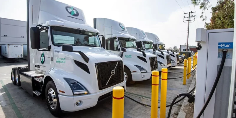 Line up of white Volvo VNR Electric trucks charging